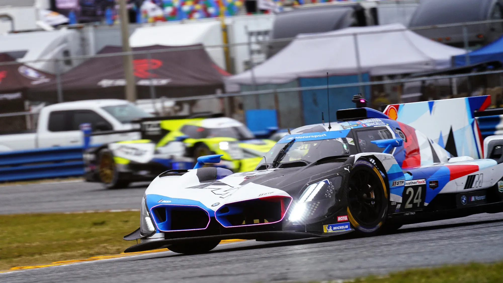 The #24 BMW on the infield at Daytona International Speedway, with an LMP2 behind.