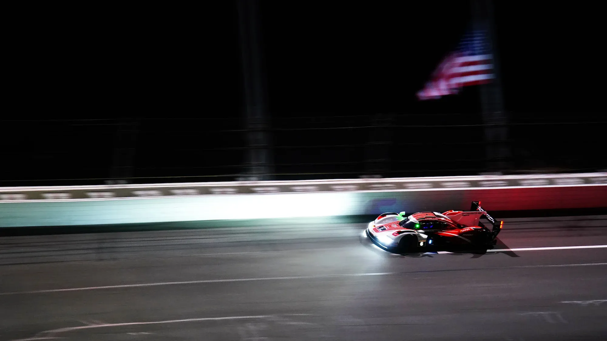 The #6 Porsche on the banking at Daytona International Speedway, at night with headlights blazing.