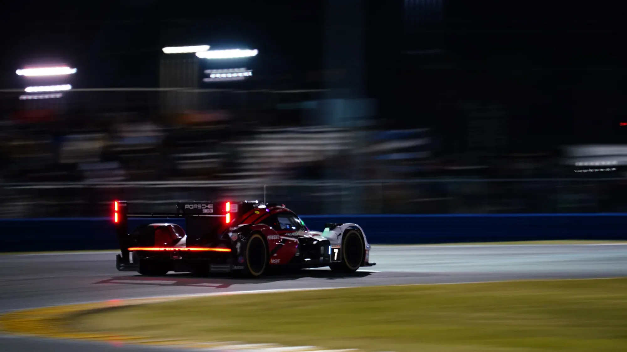 The #7 Porsche at Daytona International Speedway, taken from the rear, with rear headlights blazing red.