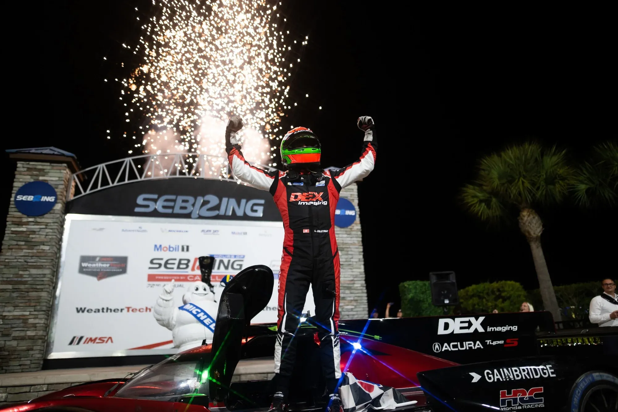 Louis Deletraz celebrating his win at Sebring in 2024 after climbing from his car, with fireworks in the background.