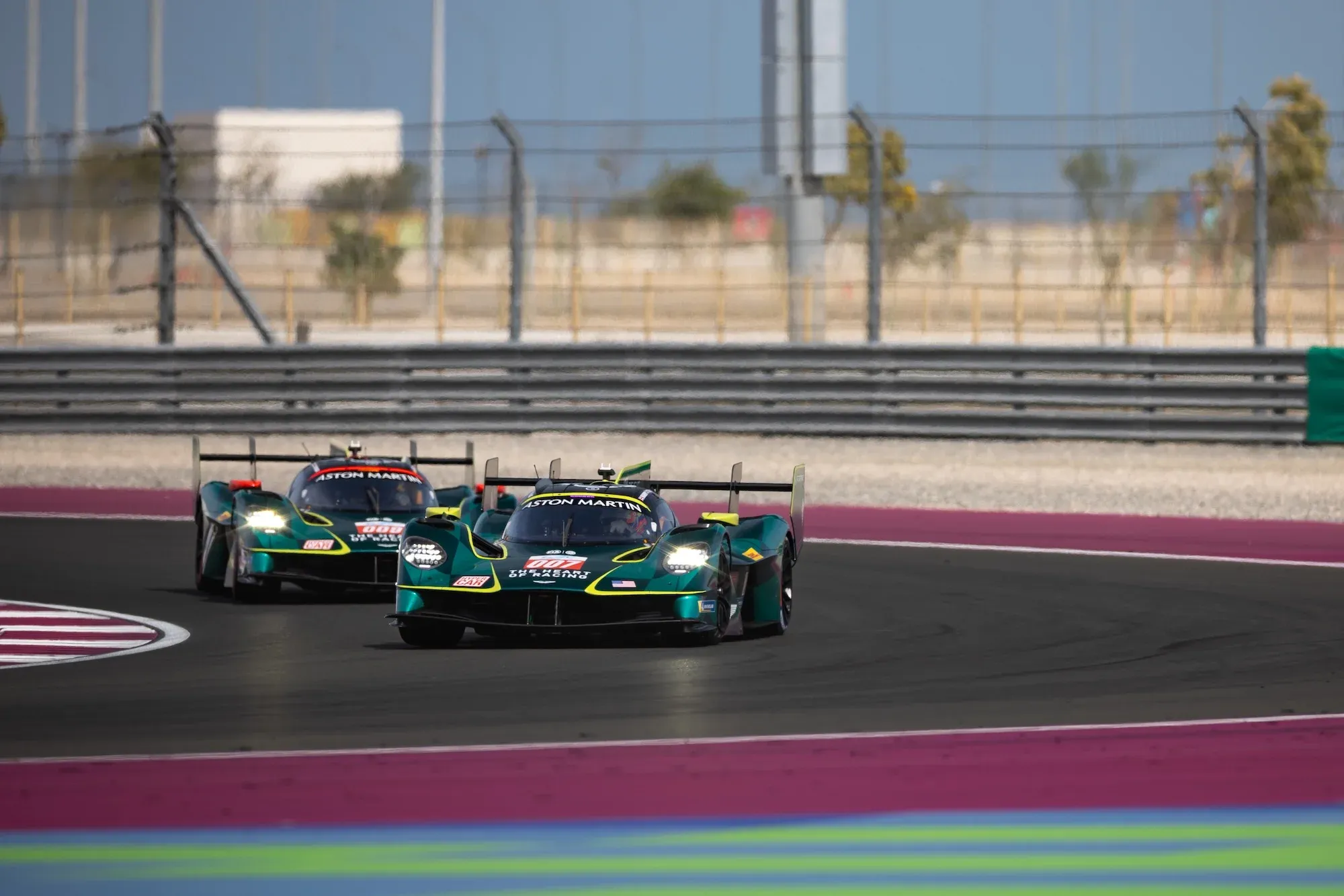 Two Aston Martin Valkyries rounding a corner at Lusail International Circuit in Qatar, in daylight.