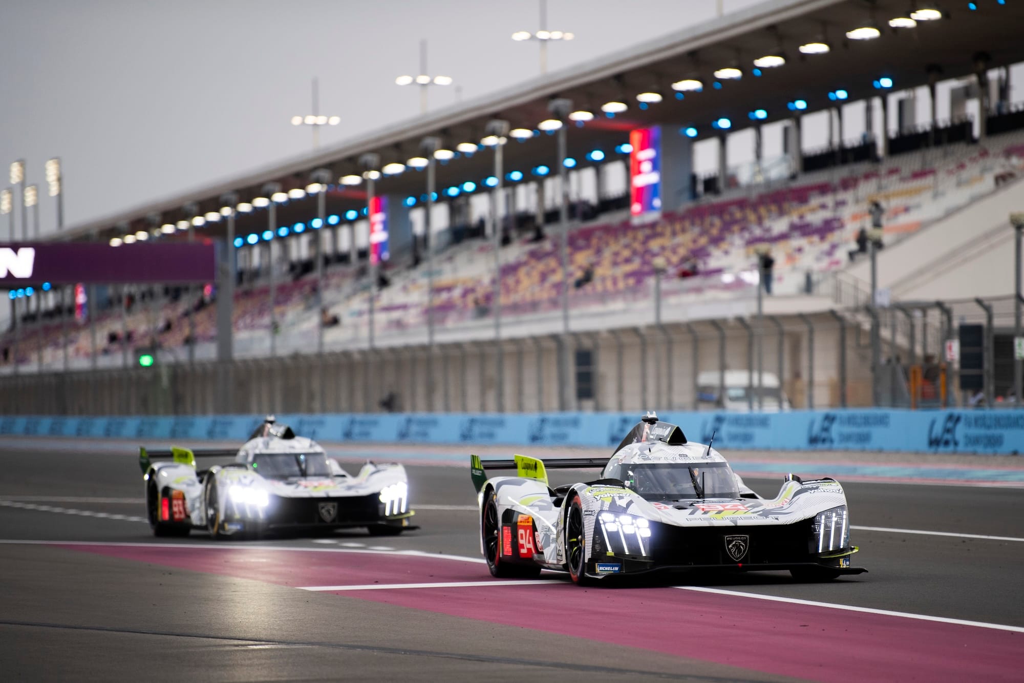 Two Peugeot 9X8s on track at Lusail International Circuit, exiting the pits.