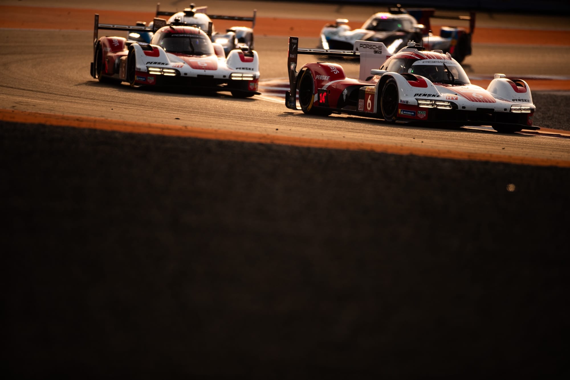 Two factory Porsche 963s on track in fading light at Lusail International Circuit, Qatar.