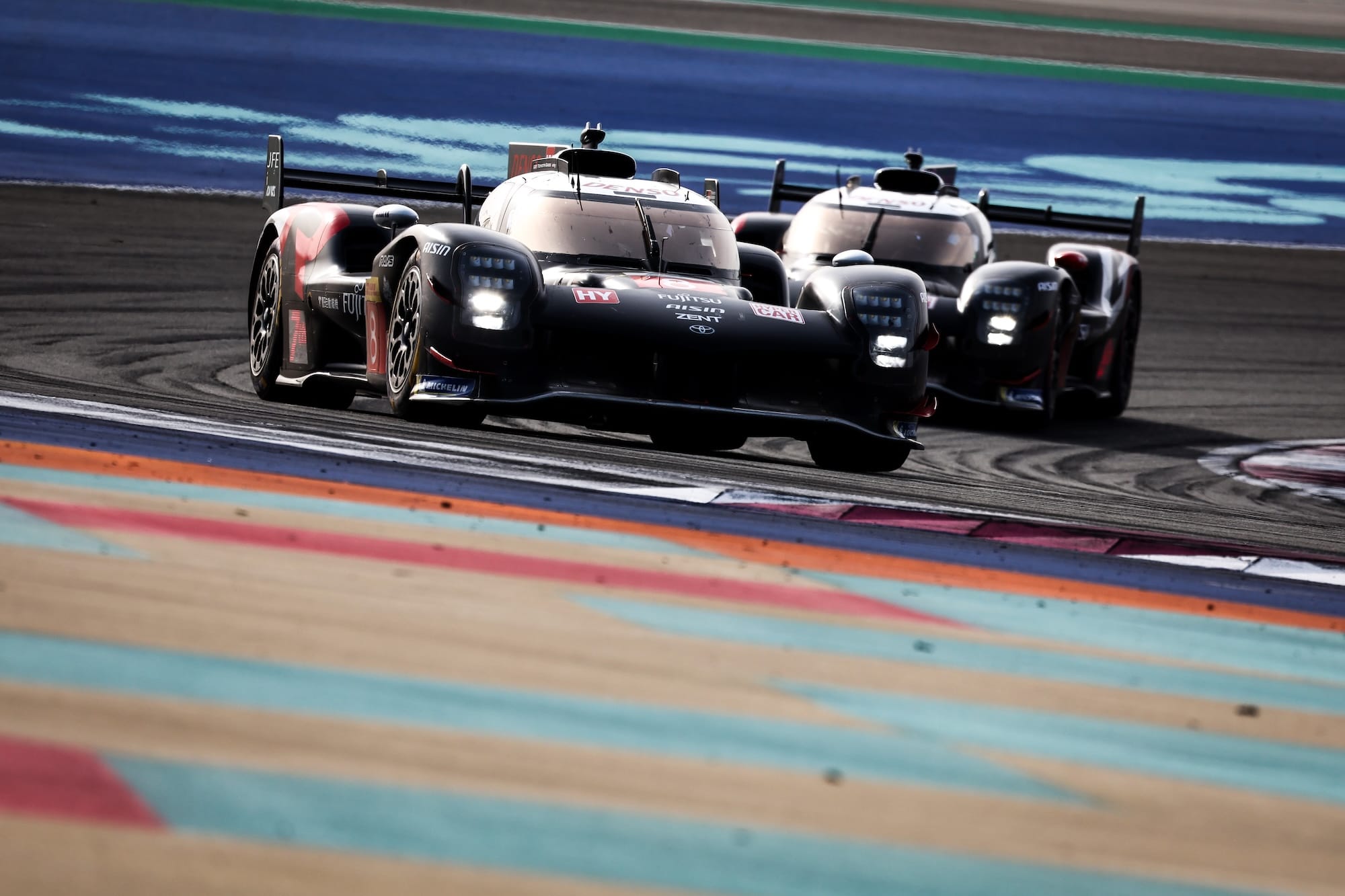 Two Toyota GR010 Hybrids on track at Lusail International Circuit, Qatar, rounding a corner.